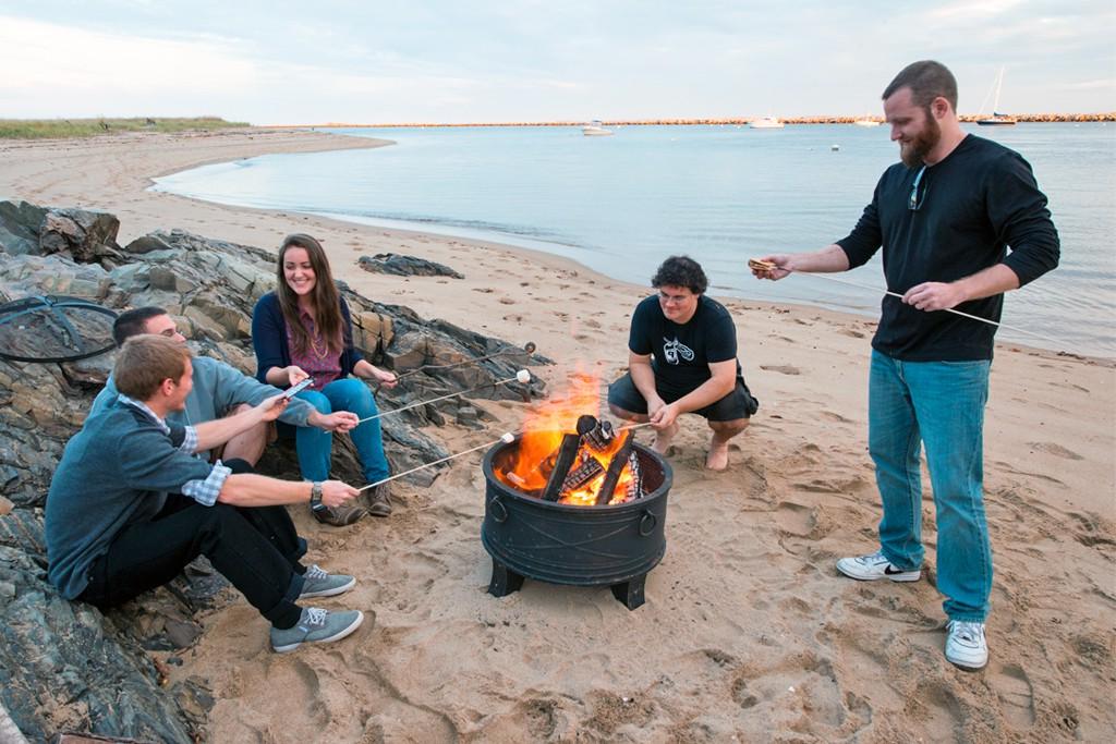 Several students sitting on the beach and having a bonfire